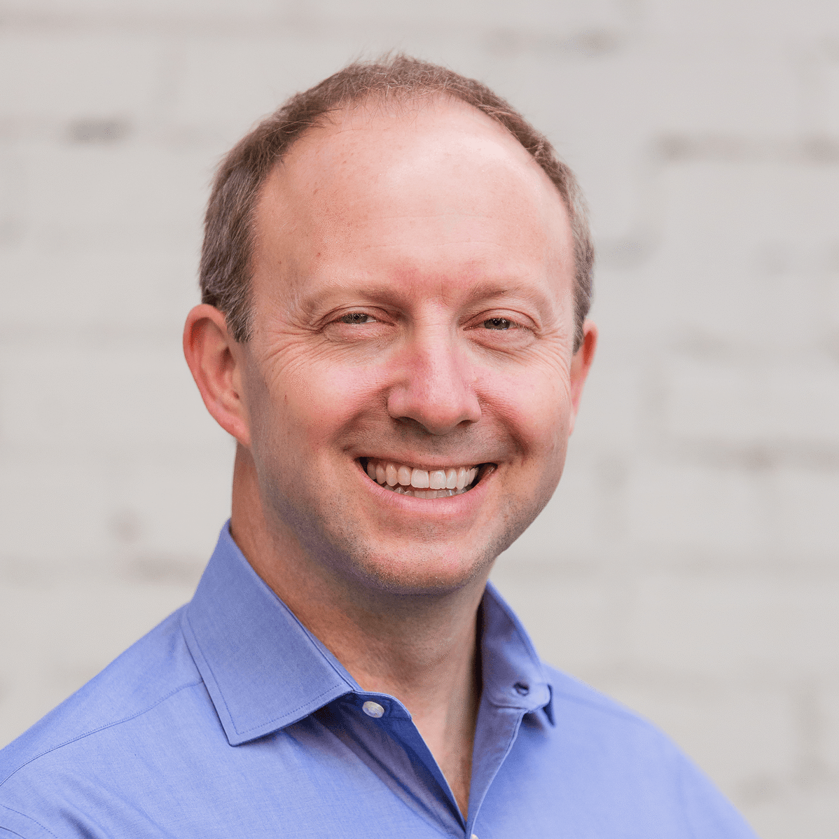 Steve Riegel smiling in a blue collared shirt against a neutral background